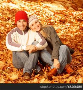 Photo of happy young family spending time together outdoors, cheerful couple sitting on floor covered dry autumnal leaves, man and woman having fun in autumn park, happiness and love concept&#xA;&#xA;