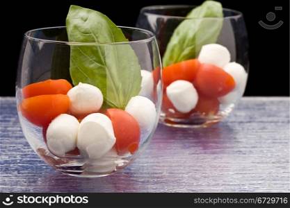 photo of italian caprese salad made of tomatoe and mozarella in glass with basil leaf