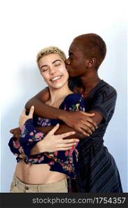 Photo of joyful ladies kissing and embracing togetherness, being of different of races, dressed in casual clothes.
