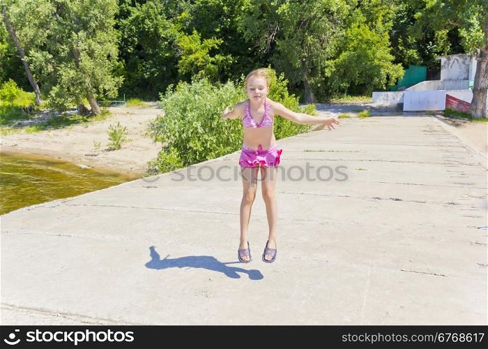 Photo of jumping girl on the riverbank in pink swimsuit