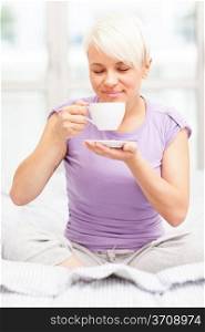 Photo of lovely blonde woman drinking coffee in her bed