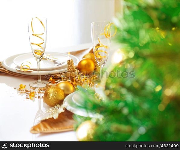 Photo of luxury Christmastime table setting, holiday dinner in restaurant, festive white dinnerware decorated with pretty golden balls and ribbons, warm candle light, green Christmas tree in room