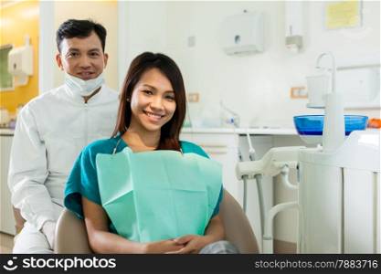 photo of male dentist with his asian patient that looking towards the camera and smiling