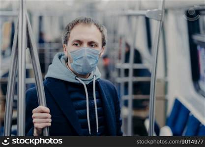 Photo of male passenger wears face mask while travels by subway during infectious disease, prevents spreading coronavirus, poses in public transport, thinks about epidemic situation in his country