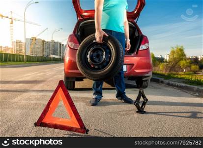 Photo of man holding spare wheel against broken car