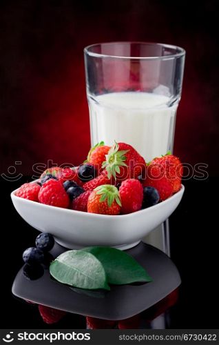 photo of milk glass with berries on red lighted background