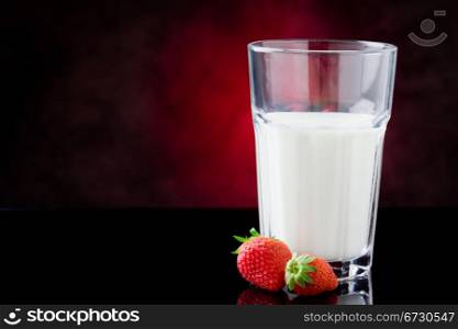 photo of milk glass with berries on red lighted background