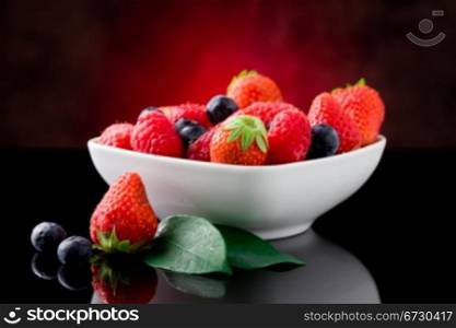 photo of mixed fresh berries on red lighted background