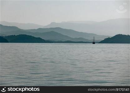 Photo of mountains and the sea landscape. Overcast weather. Travel by sailboat. Summer vacation in the sea. Turkey. Sailboat in the sea with moutains landscape