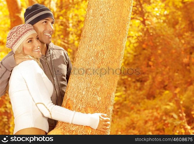 Photo of of happy couple playing game in autumn park, closeup portrait of two loving people hugging tree, cute woman and handsome guy wearing stylish warm hats, happiness and affection concept&#xA;&#xA;