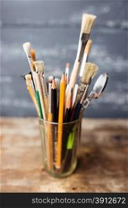 Photo of paint brushes in a glass standing on old wooden table, small dof