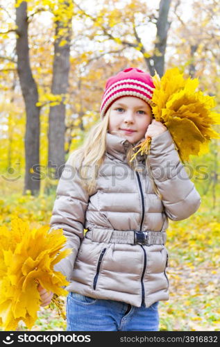 Photo of playing girl with two bouquets of sheets in autumn