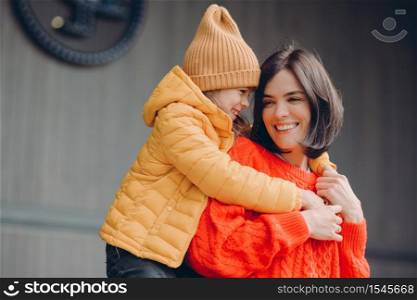 Photo of positive lovely mother and small child embrace friendly, have good relationships, demonstrate truthful feelings, wear fashionable outfit, smile positively. Family and children concept