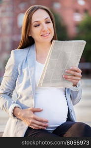 Photo of pregnant business woman reading the newspaper on a bench