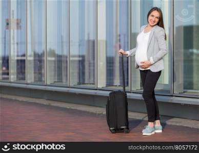 Photo of pregnant business woman with suitcase in the city