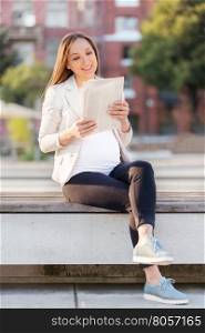 Photo of pregnant businesswoman reading the newspaper on a bench
