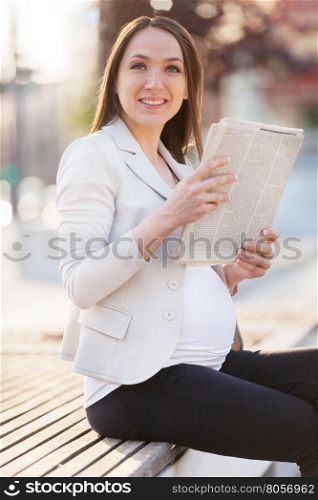 Photo of pregnant businesswoman reading thenewspaper on a bench