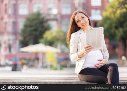 Photo of pregnant businesswoman reading thenewspaper on a bench