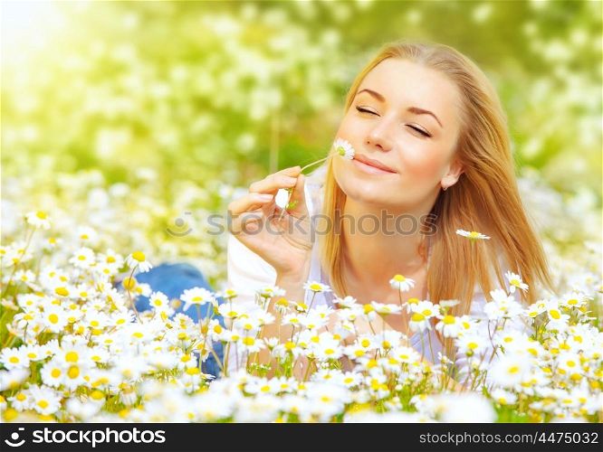Photo of pretty blonde woman lying down in chamomile field, cute female enjoying smell of daisy, sweet teenager girl with closed eyes relaxed on flowers meadow, spring nature, having fun outdoor