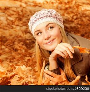 Photo of pretty girl lying down on the ground covered dry autumnal foliage, cute young lady having fun in fall park, nice female wearing stylish hat, attractive woman holding old tree leaf in hand&#xA;