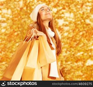Photo of pretty happy woman with shopping bags in park, smiling cute blond girl enjoying of new purchase over autumn foliage background, fashion and style lifestyle, spending money concept