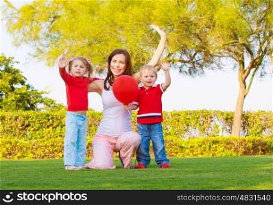 Photo of pretty mother with two cute kids raised hands up and enjoying sunny day, happy young family waving hand in spring park, woman with daughter and son having fun outdoors, love concept