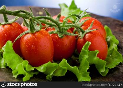 photo of red tomatoes with water drops over lettuce bed