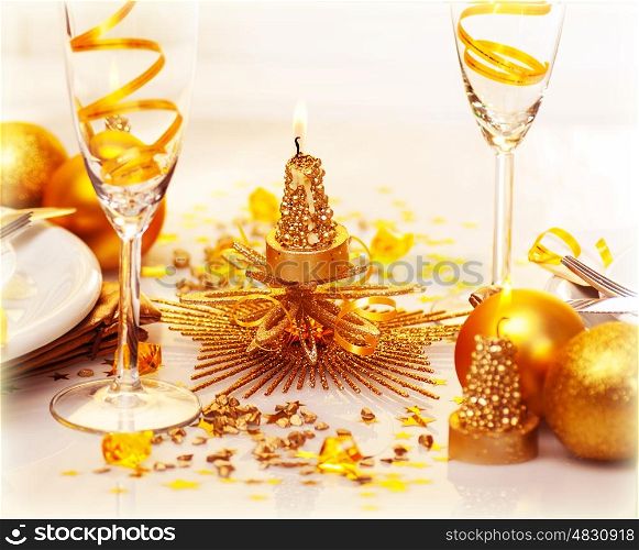 Photo of romantic Christmas dinner, two glasses for champagne adorned with golden ribbon, beautiful little candle, gold shiny bauble, holiday table setting, New Year decorations