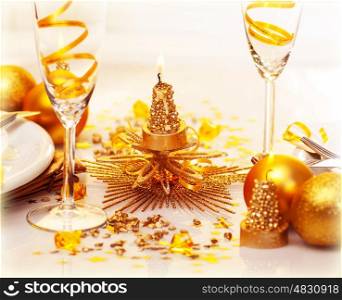 Photo of romantic Christmas dinner, two glasses for champagne adorned with golden ribbon, beautiful little candle, gold shiny bauble, holiday table setting, New Year decorations