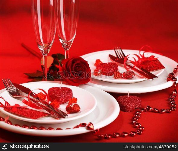 Photo of romantic dinner table setting, holiday banquet, white festive dinnerware on red tablecloth decorated with fresh rose flower and heart-shaped candles, Valentine day, two wineglasses