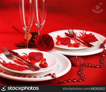 Photo of romantic dinner table setting, holiday banquet, white festive dinnerware on red tablecloth decorated with fresh rose flower and heart-shaped candles, Valentine day, two wineglasses