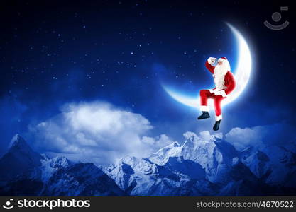 photo of santa claus sitting on the moon. Photo of Santa Claus sitting on shiny moon above winter forest