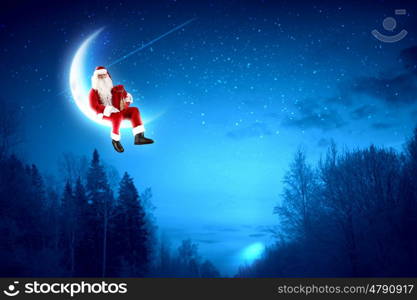 photo of santa claus sitting on the moon. Photo of Santa Claus sitting on shiny moon above winter forest