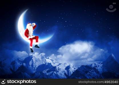 photo of santa claus sitting on the moon. Photo of Santa Claus sitting on shiny moon above winter forest