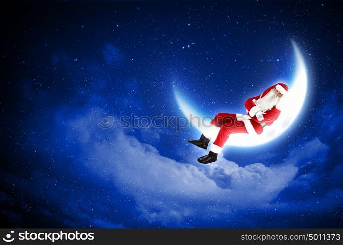 photo of santa claus sitting on the moon. Photo of Santa Claus sitting on shiny moon above winter forest