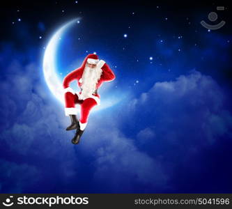 photo of santa claus sitting on the moon. Photo of Santa Claus sitting on shiny moon above winter forest