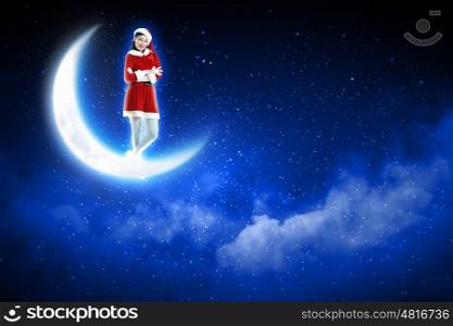 photo of santa girl sitting on the moon. Photo of Santa girl standing on shiny moon above winter forest