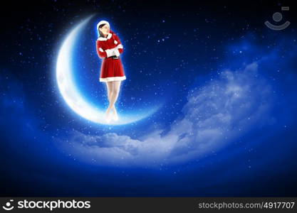 photo of santa girl sitting on the moon. Photo of Santa girl standing on shiny moon above winter forest