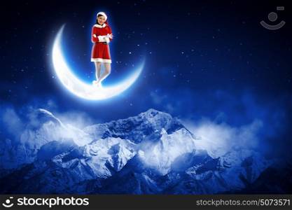 photo of santa girl sitting on the moon. Photo of Santa girl standing on shiny moon above winter forest