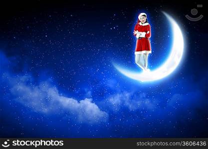Photo of Santa girl standing on shiny moon above winter forest