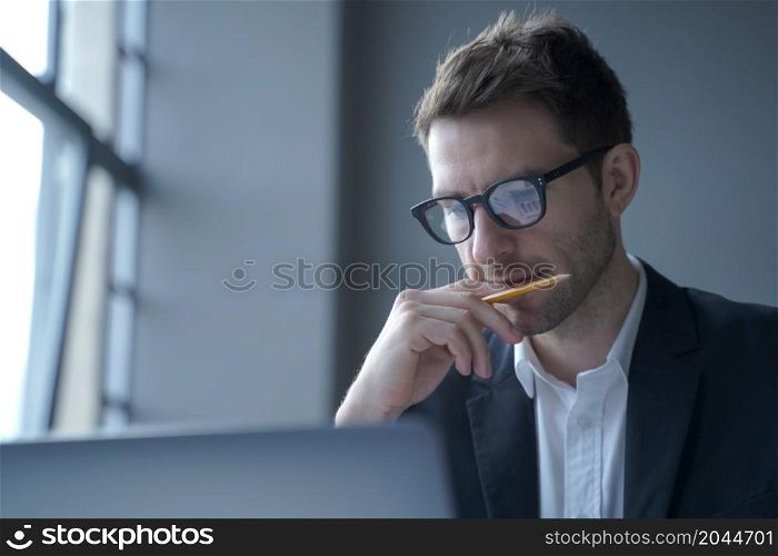 Photo of serious german man executive dressed in elegant formal clothes looking at laptop screen, browsing internet web page while working in modern office, close up. Business people at work concept. Serious german man executive dressed in formal clothes looking at laptop screen browsing internet