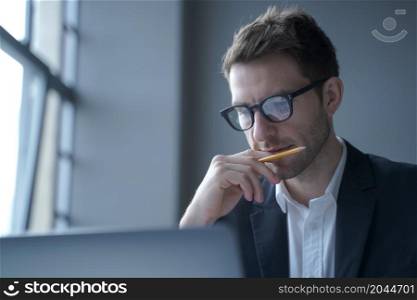 Photo of serious german man executive dressed in elegant formal clothes looking at laptop screen, browsing internet web page while working in modern office, close up. Business people at work concept. Serious german man executive dressed in formal clothes looking at laptop screen browsing internet