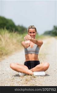 Photo of smiling blonde woman doing stretching exercises on a field street
