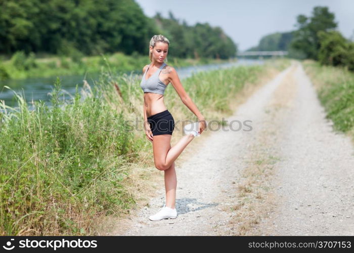 Photo of smiling blonde woman doing stretching exercises on a field street