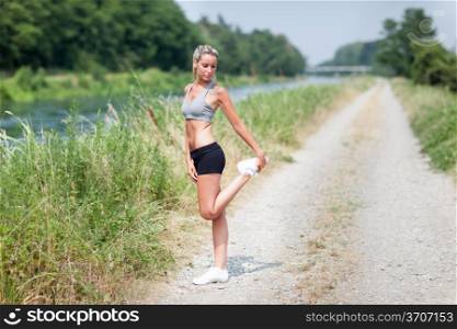Photo of smiling blonde woman doing stretching exercises on a field street