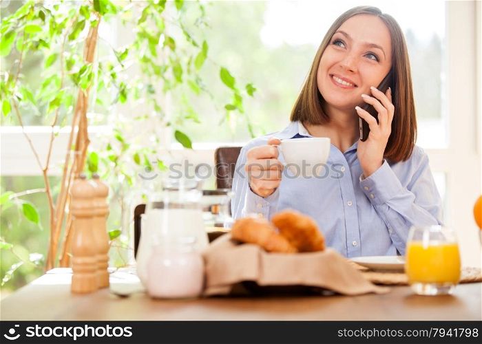 Photo of smiling brunette businesswoman phoning while having breakfast
