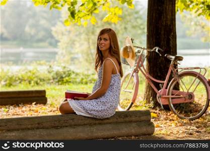 photo of smiling brunette woman sitting in the park and reading a book
