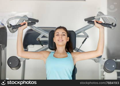 Photo of smiling caucasian brunette training her upper body in gym