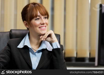 photo of smiling caucasian businesswoman sitting on her chair in the office and looking at the screen