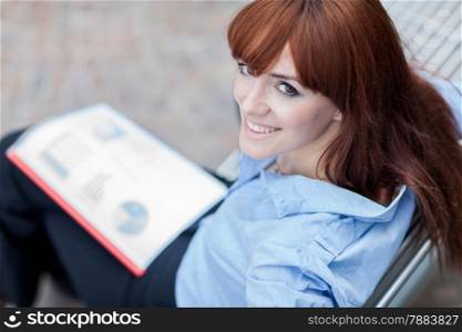 Photo of smiling caucasian businesswoman with charts in her hands sitting outdoor